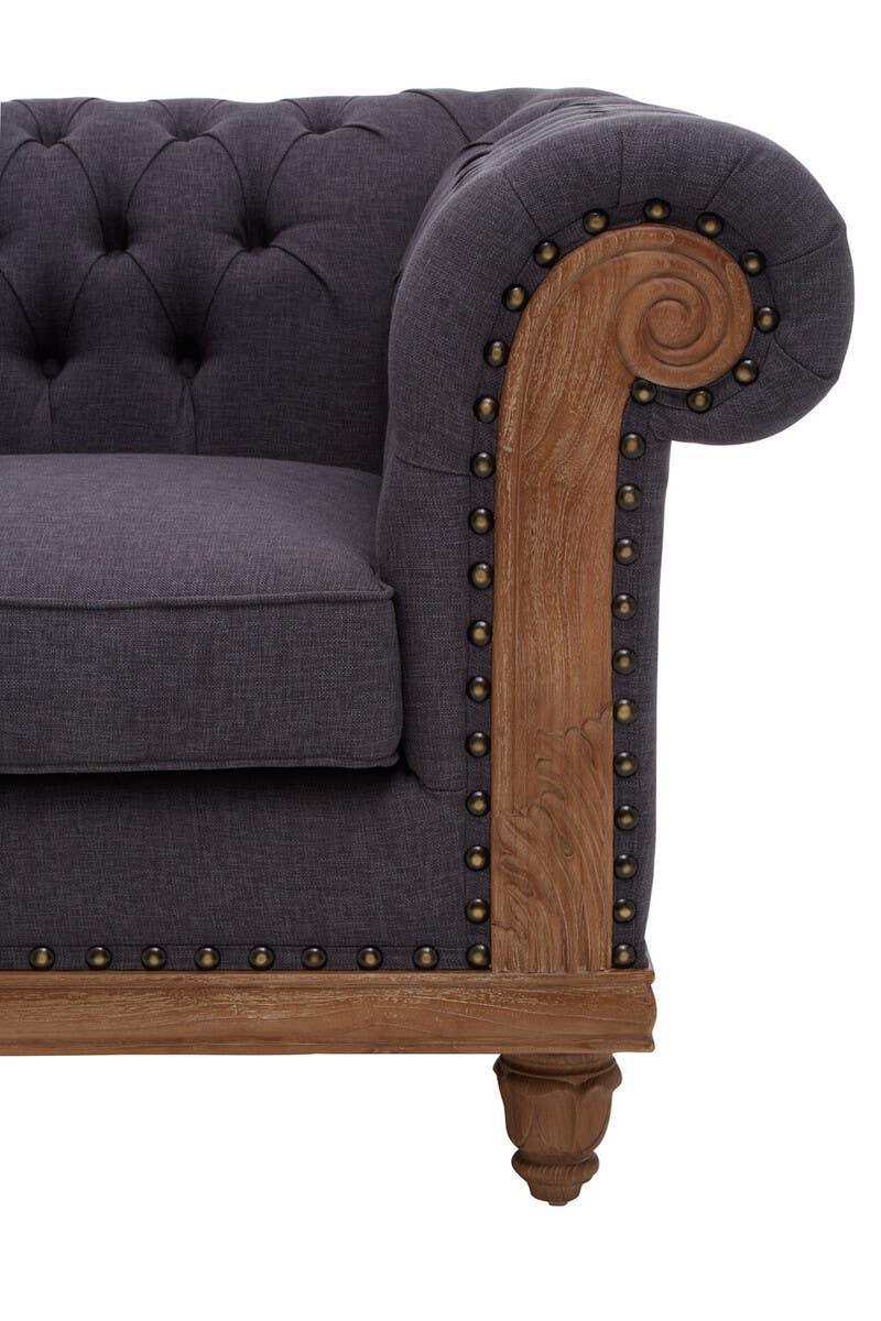 Dark grey fabric sofa with button-tufted back, wooden scroll armrest, and brass stud detailing