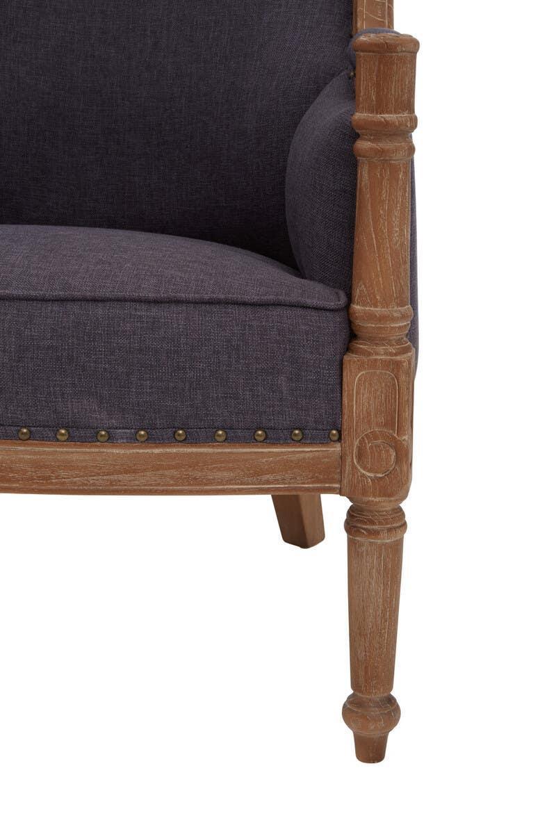 Grey upholstered armchair with carved wooden leg and brass stud detail