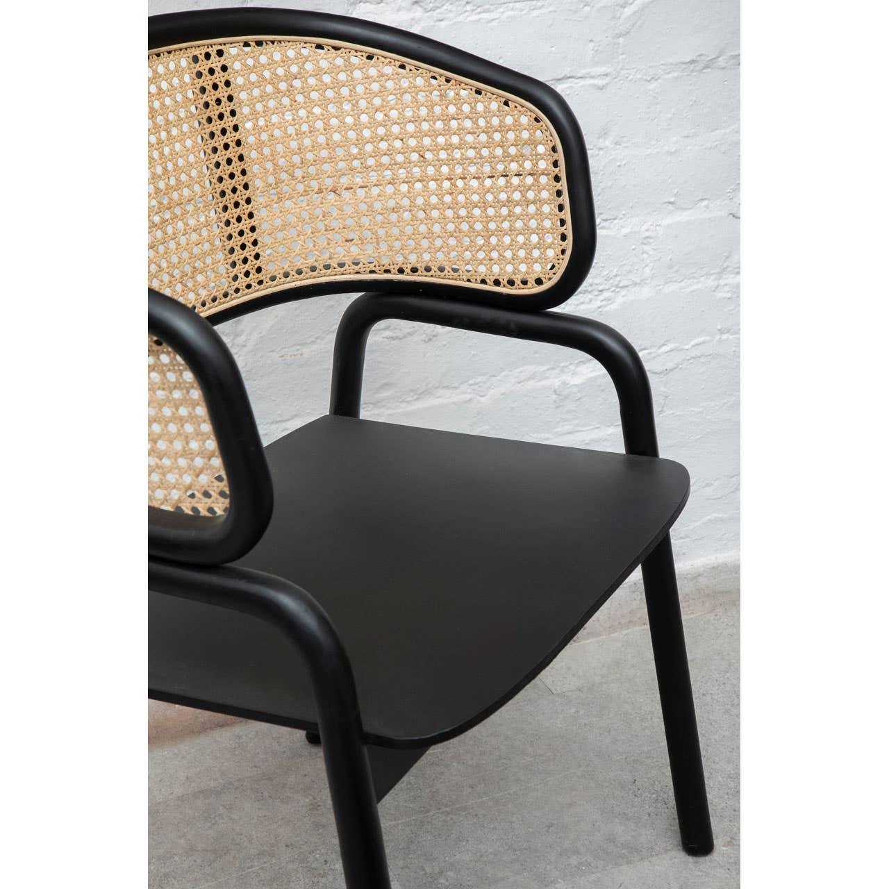 Black wooden dining chair with cane rattan backrest against white wall