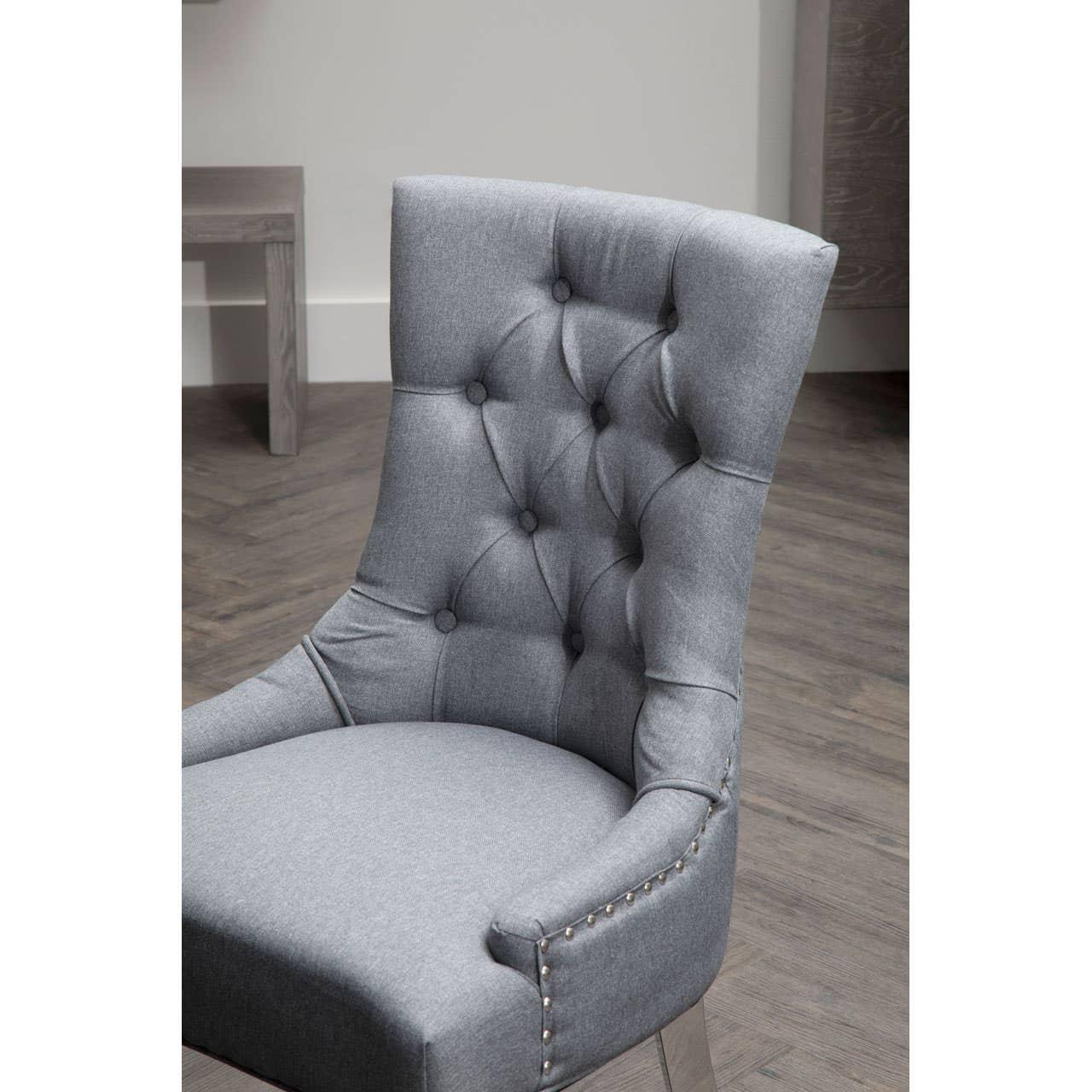 Grey fabric dining chair with button-tufted backrest and silver stud detailing on armrest