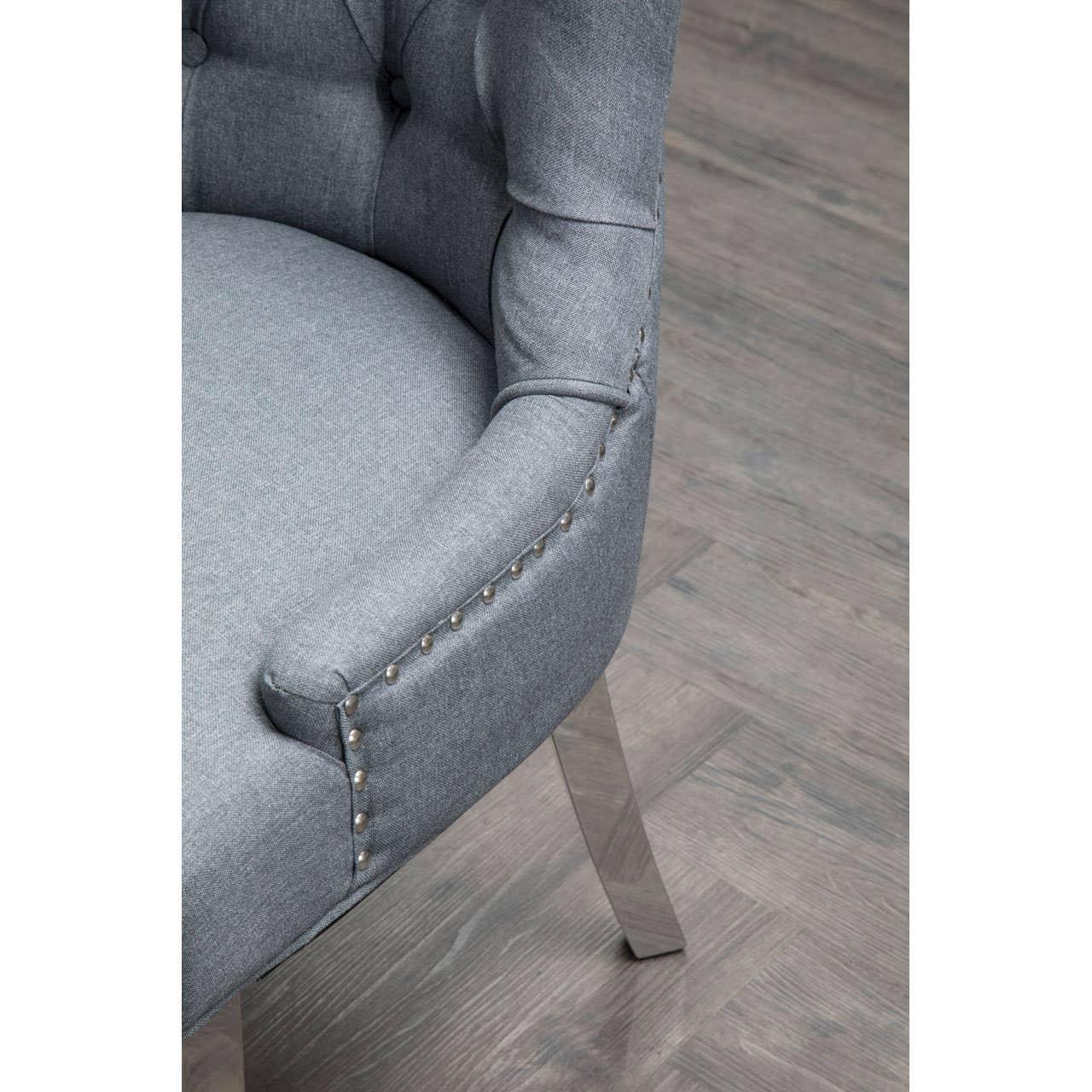 Grey upholstered dining chair with buttoned backrest and metal stud detailing on wooden floor
