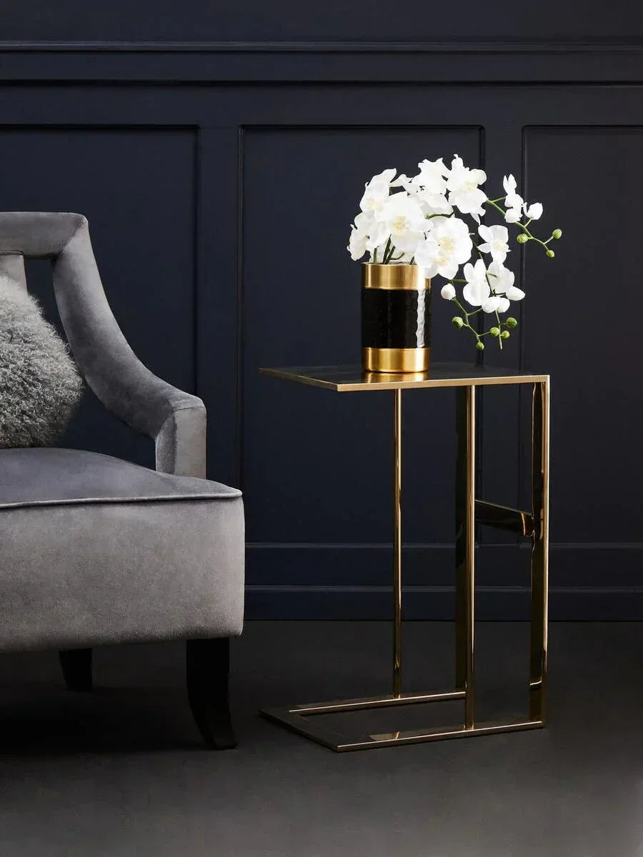 Gold metal side table with vase of white flowers beside grey velvet armchair