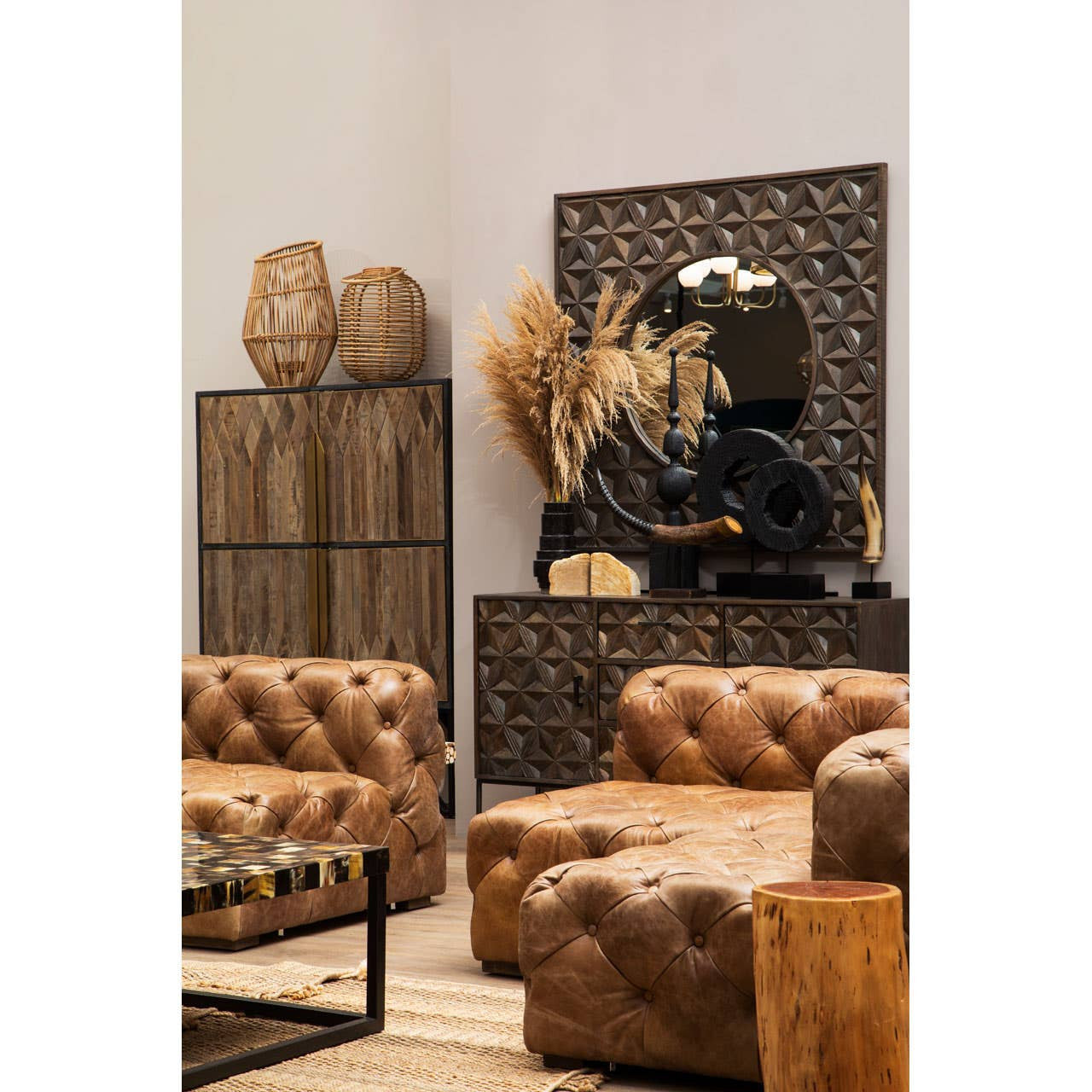 Textured wooden cabinet with a geometric pattern, placed against a light-colored wall. The cabinet features decorative items on top, including vases and dried plants. In the foreground, there are brown tufted sofas and a coffee table, creating a cozy living space ambiance