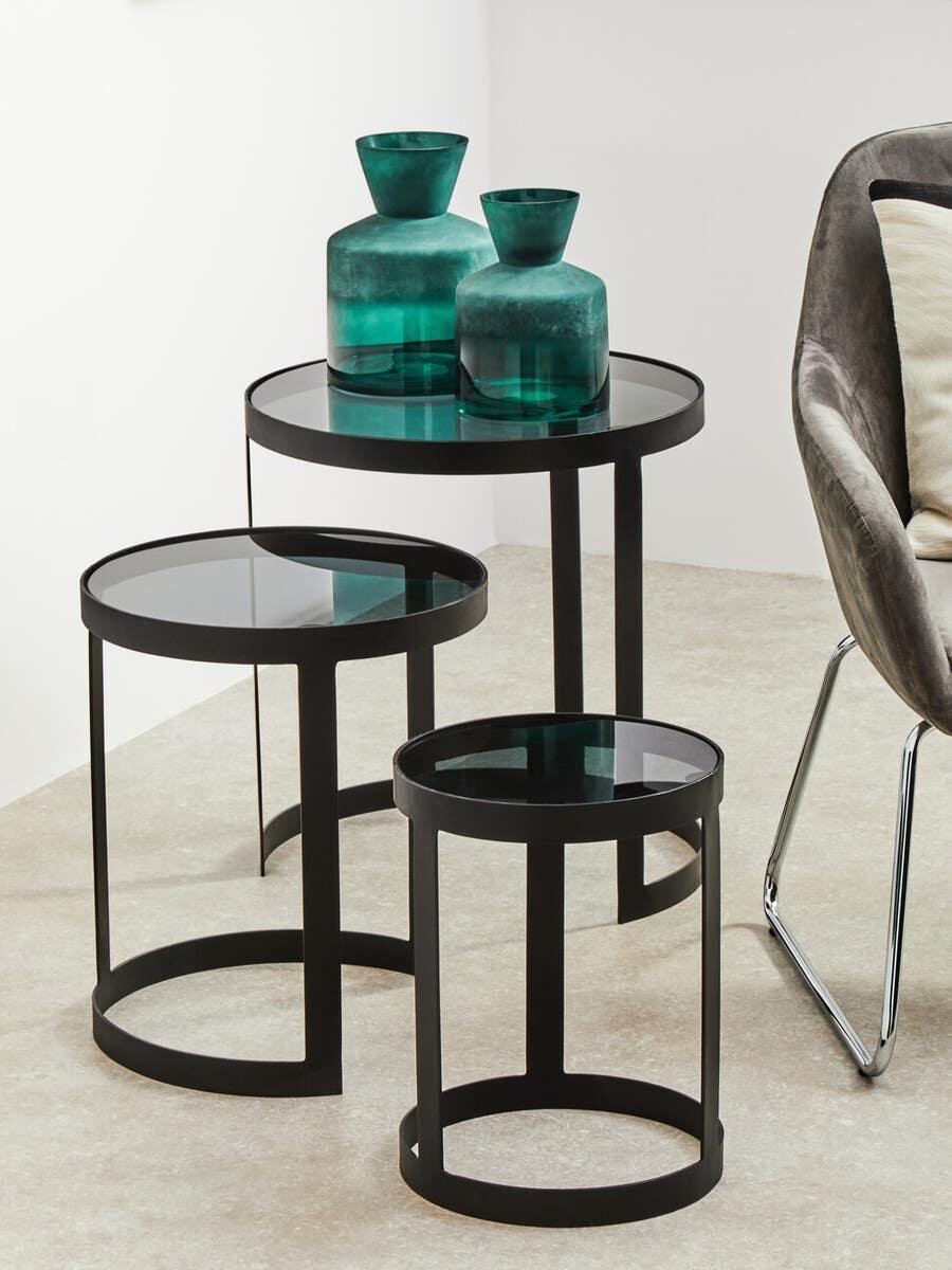 Set of three black metal and glass nesting tables with teal glass vases in modern living room