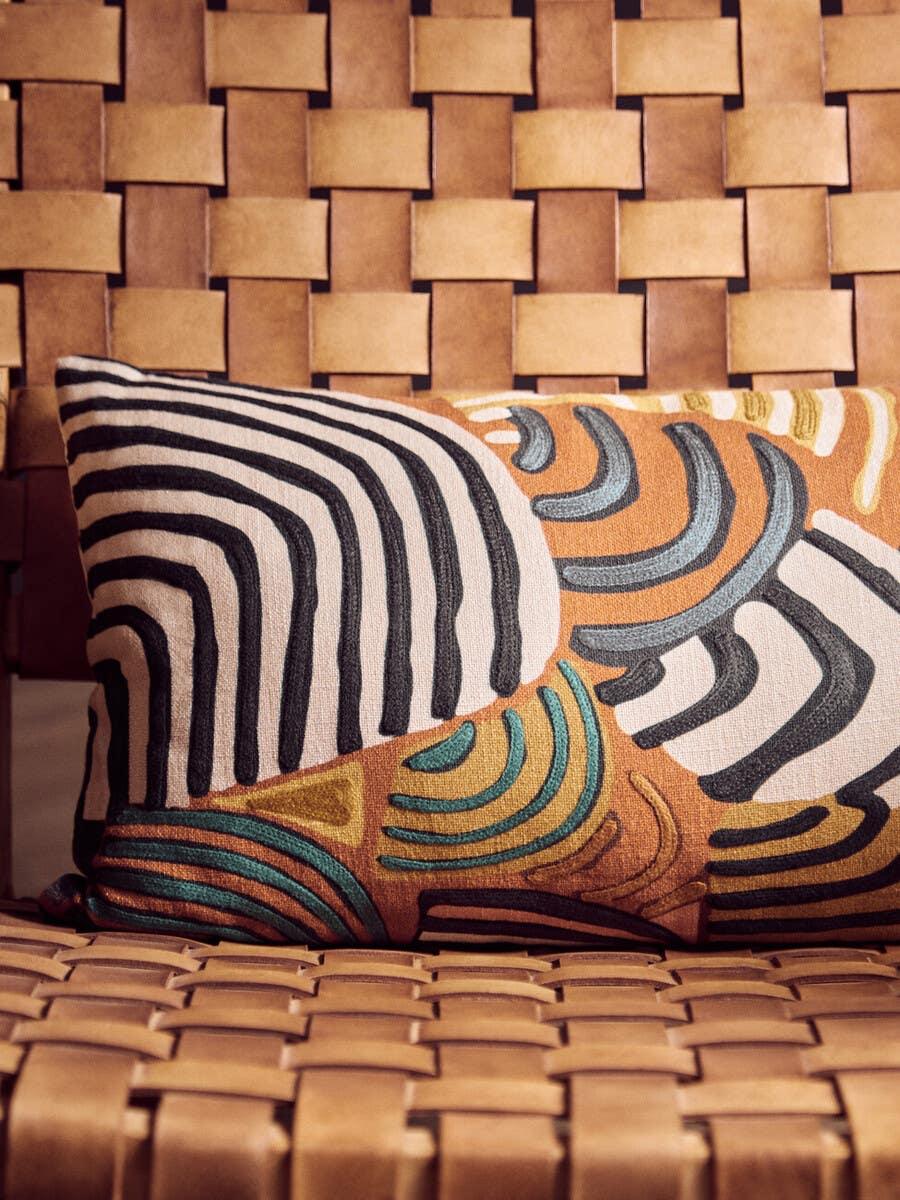 Tan leather woven chair with geometric embroidered cushion in earthy tones