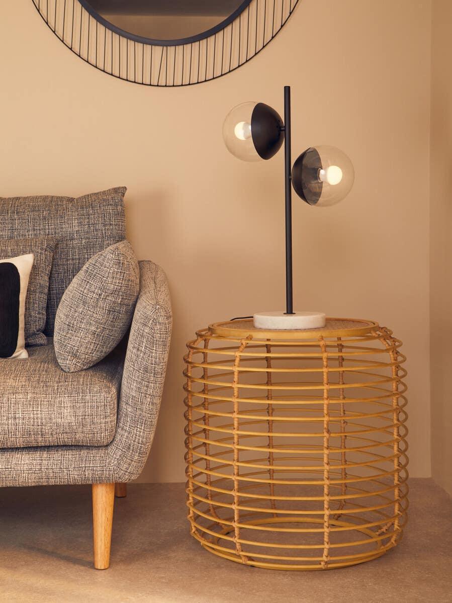 Rattan side table with modern table lamp beside grey fabric sofa in living room corner