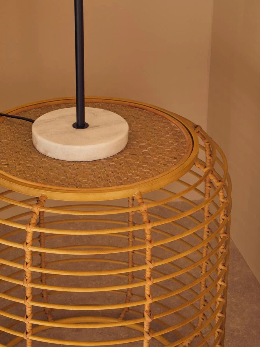 Rattan side table with woven top and round marble lamp base in neutral room corner