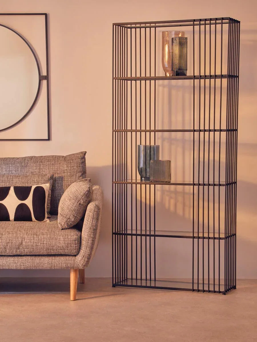 Modern black metal shelving unit with glass shelves beside grey fabric sofa in living room
