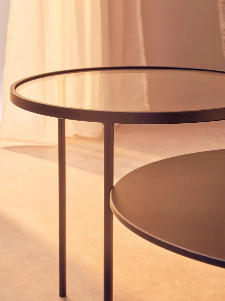 Round glass top coffee table with black metal frame in warm indoor lighting