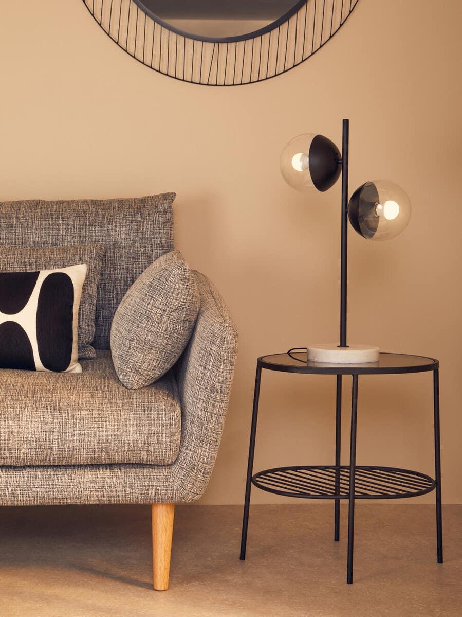 Grey fabric sofa with patterned cushion beside black metal side table and modern table lamp