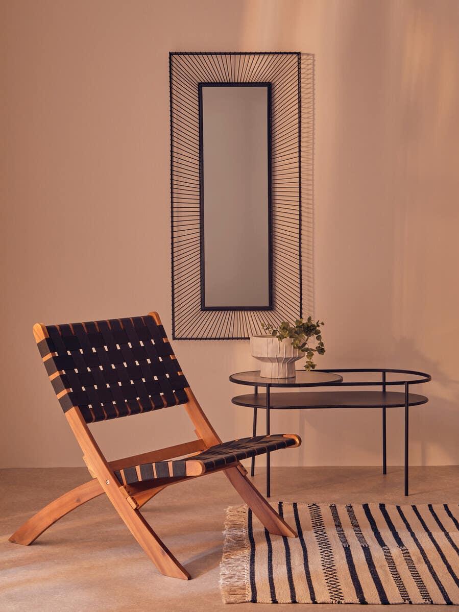 Wooden lounge chair with black woven seat beside glass side table and striped rug