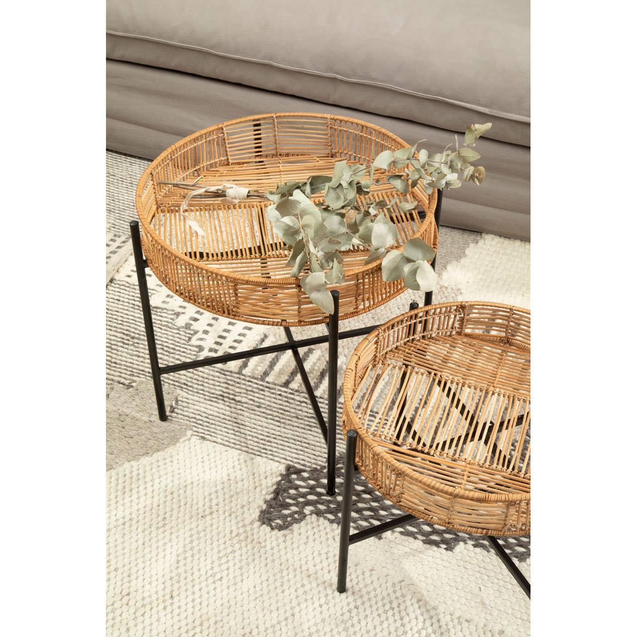 Round rattan side tables with black metal legs on patterned rug, sofa in background