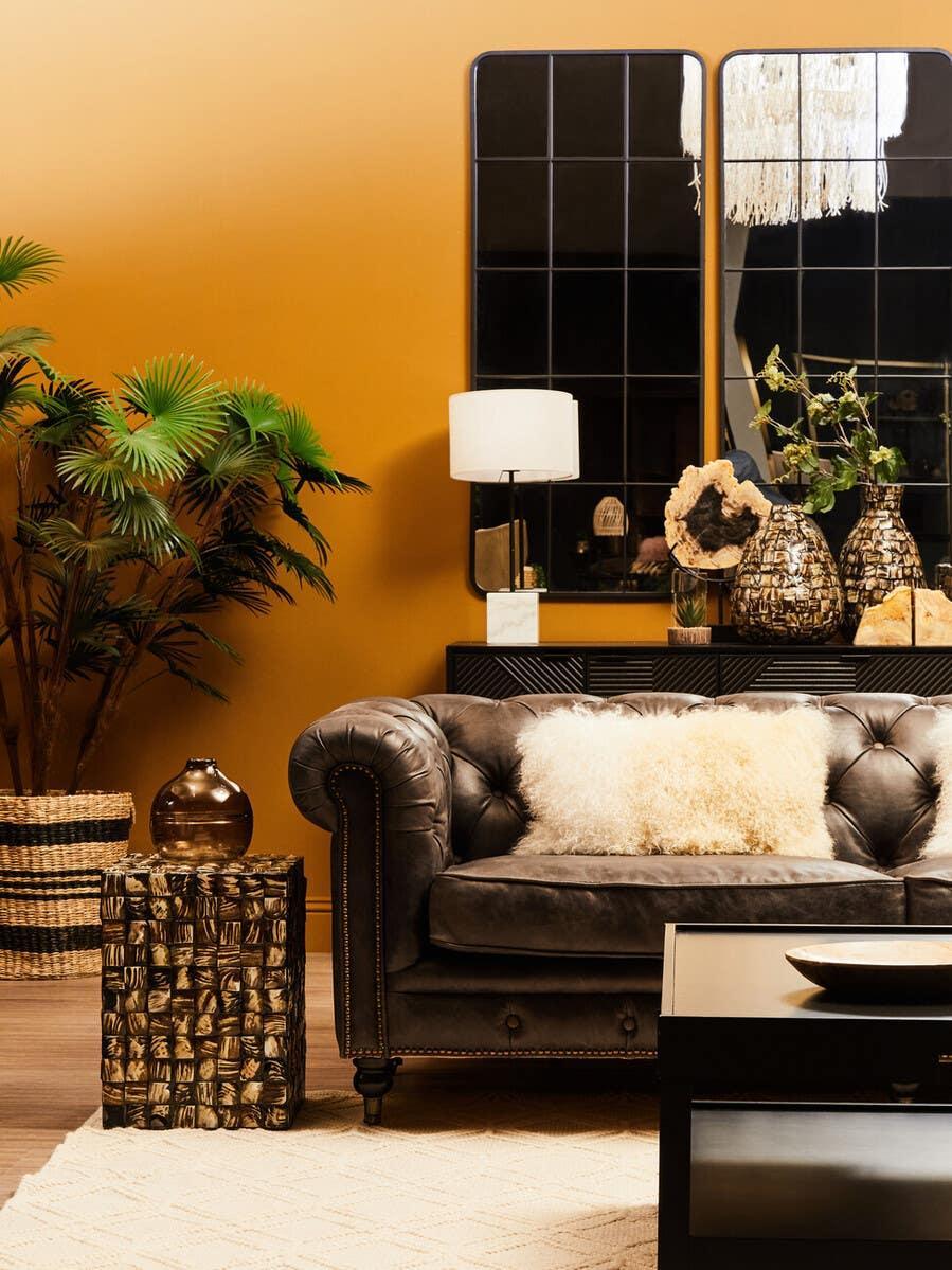 Dark leather sofa with cream cushion, geometric side table and indoor plants in modern living room