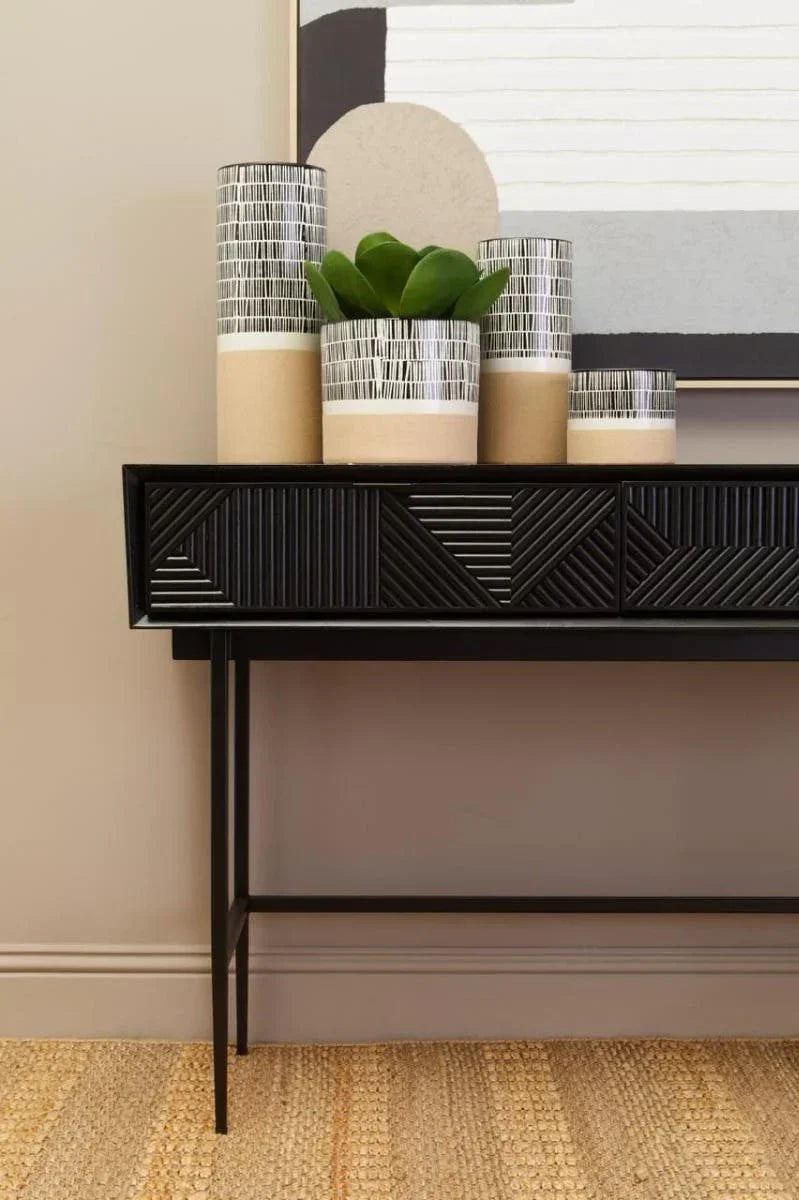 Black console table with patterned front and decorative ceramic vases, plant and wall art