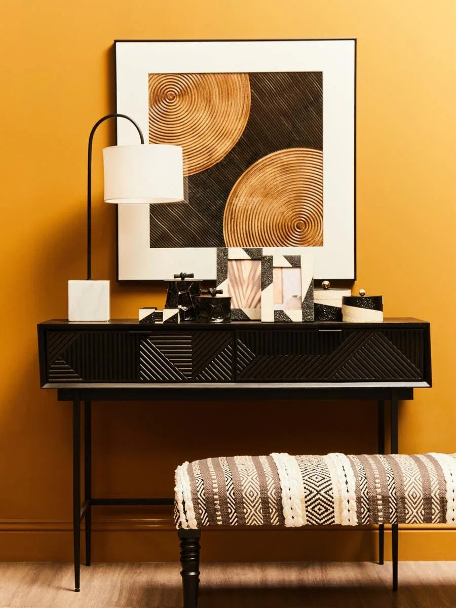 Black console table with geometric drawer fronts, table lamp, decor accents, and abstract art