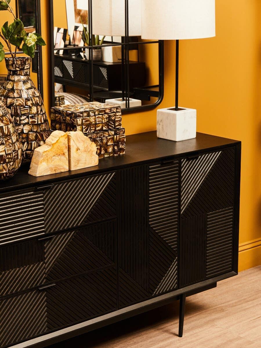 Black geometric sideboard with decorative vases, marble lamp, and mirror against yellow wall