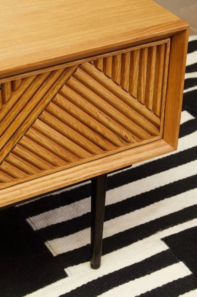 Wooden coffee table with geometric carved drawer and black legs on striped rug