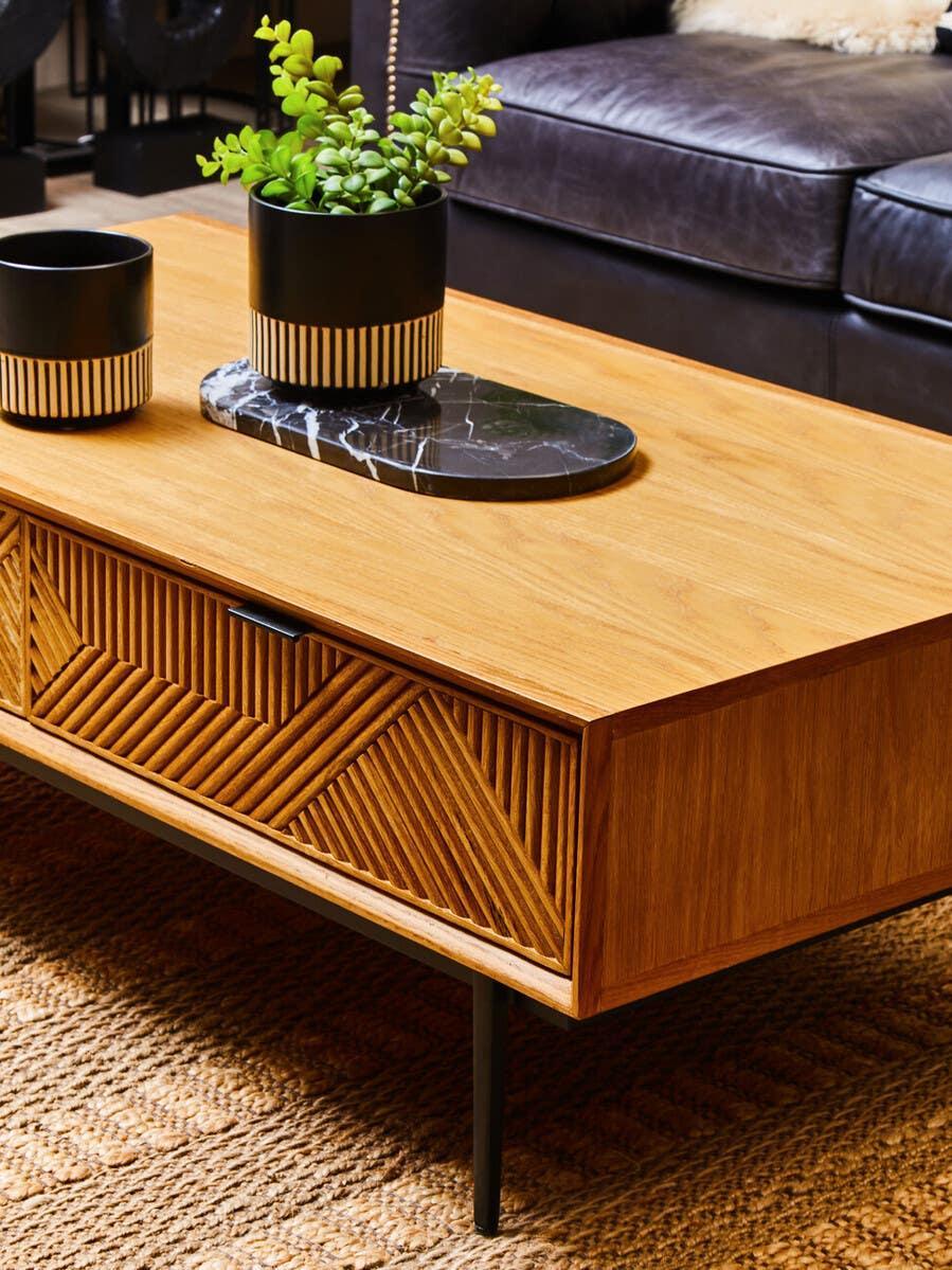 Wooden coffee table with textured drawer front, black legs, and decorative plant pot