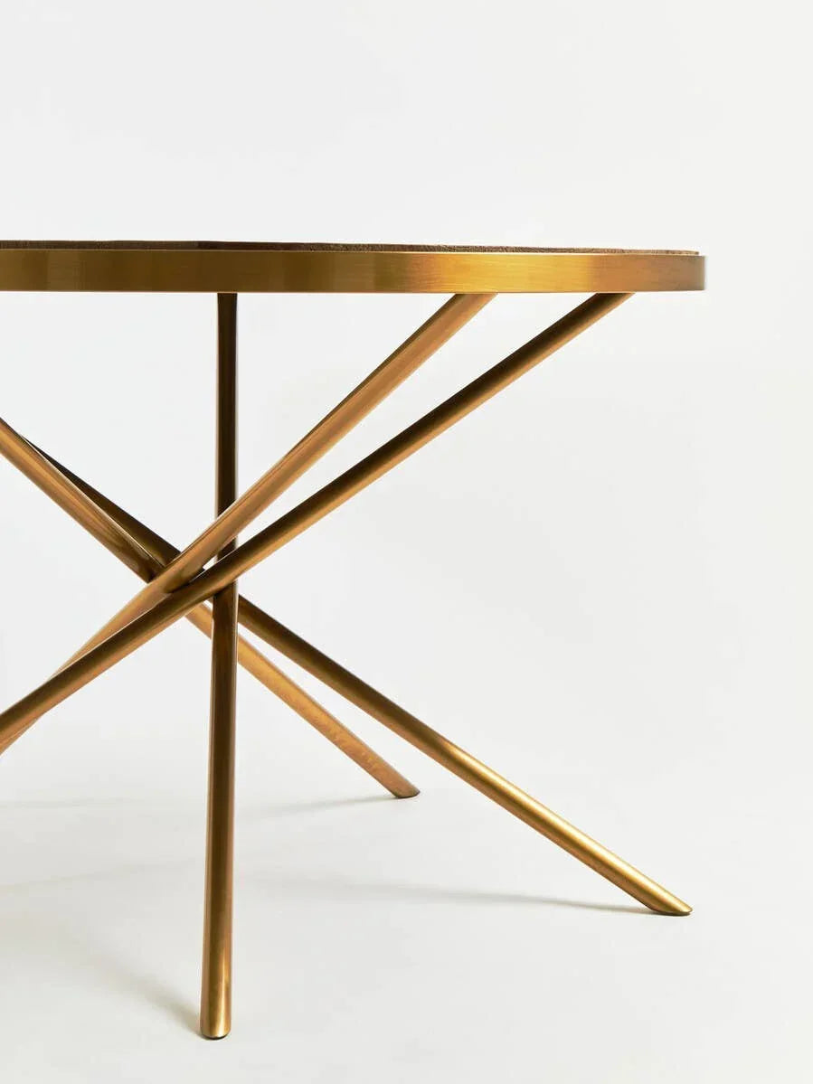 Round gold dining table with crossed metal legs on white background