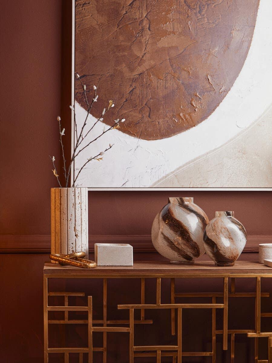 Metal console table with marble vases, decorative branches, abstract wall art background