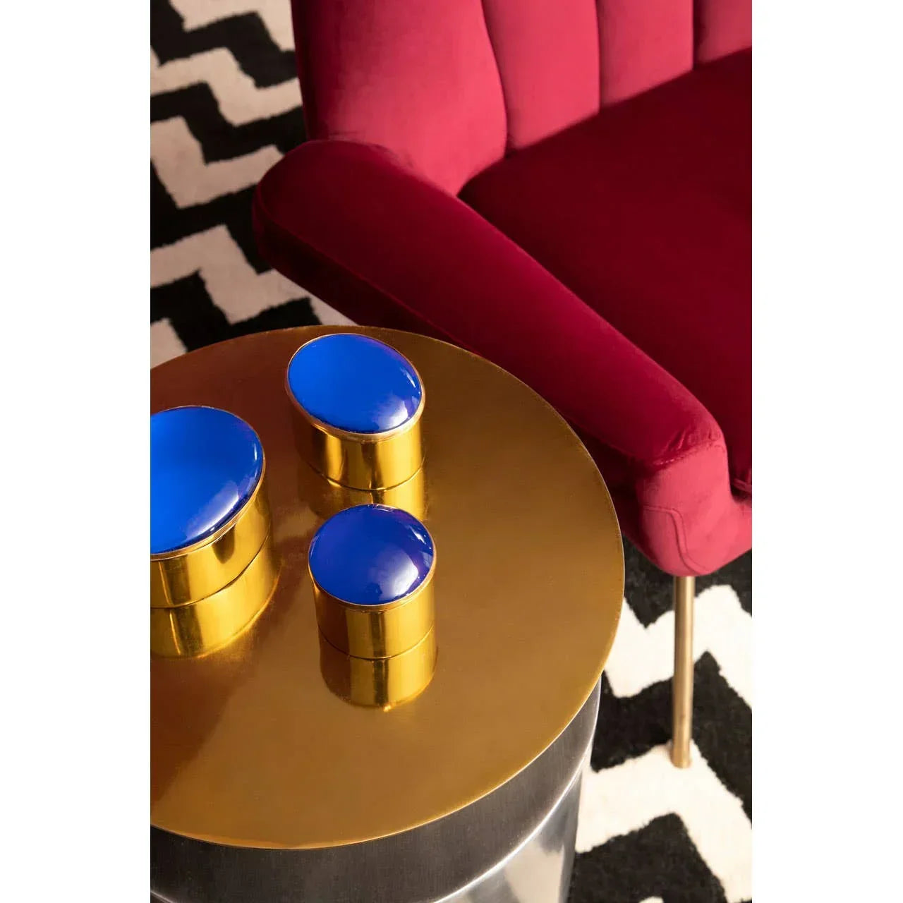 Gold round side table with three blue lidded storage jars beside a red velvet sofa