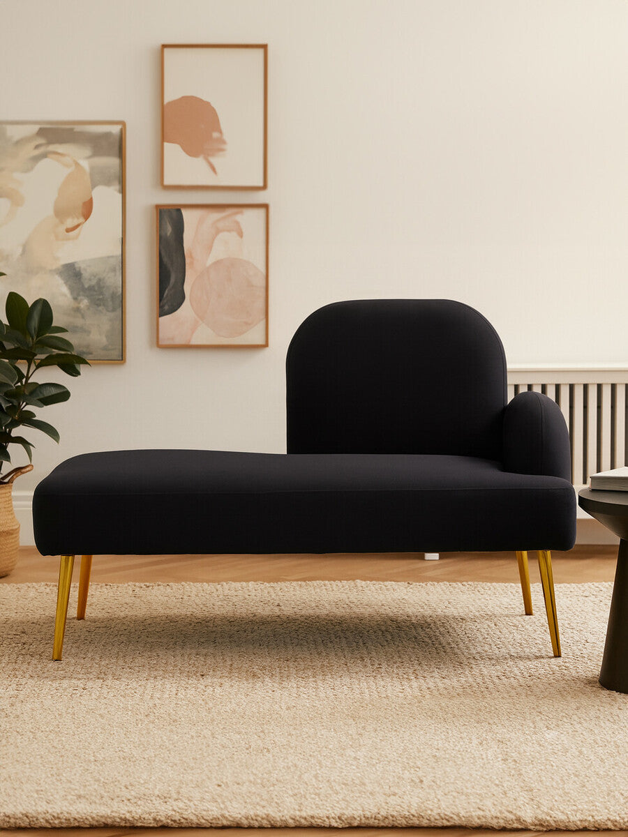 A sleek black chaise longue with a right-hand armrest, featuring a modern design and wooden legs. The chaise is positioned on a light-colored rug, with abstract wall art and a potted plant in the background, creating a stylish living space ambiance