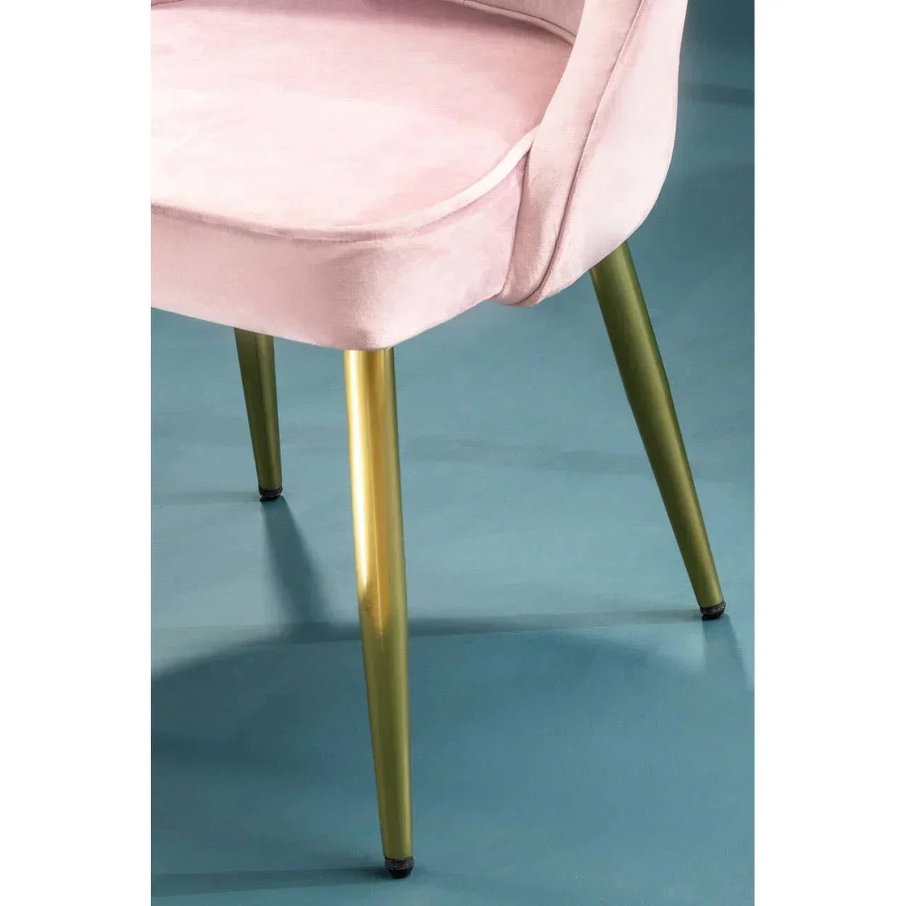 Pink velvet chair with gold metal legs on blue floor, close-up of seat and legs