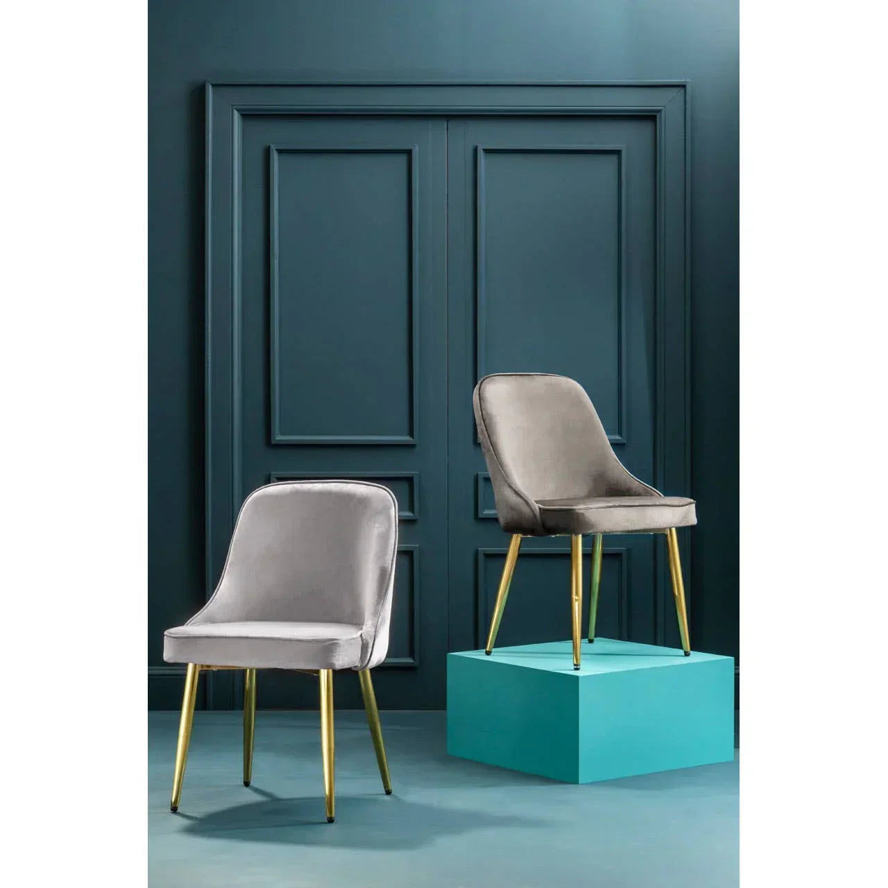 Pair of grey velvet dining chairs with gold metal legs against blue panel wall