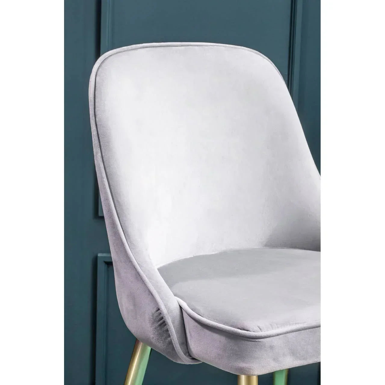Grey velvet dining chair with gold metal legs against a dark teal wall