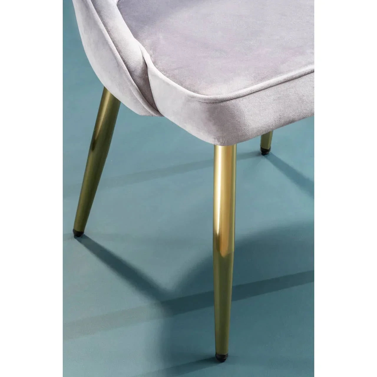 Grey velvet dining chair with gold metal legs on blue floor, close-up view