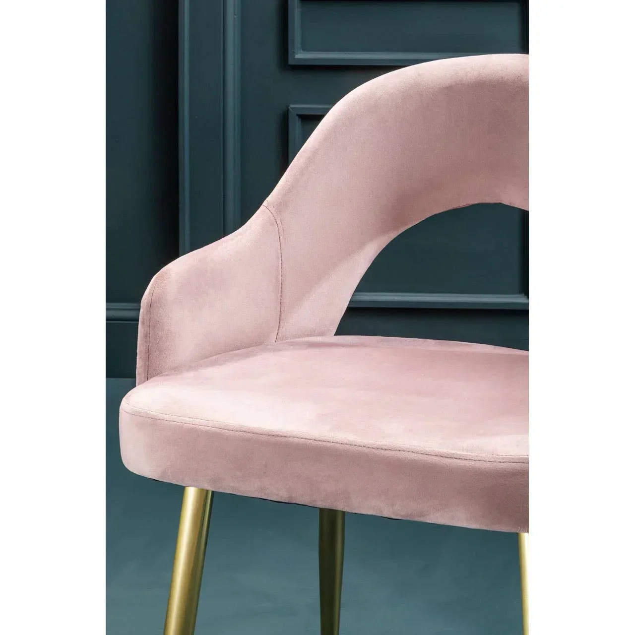 Pink velvet dining chair with curved backrest and gold metal legs against dark panel wall