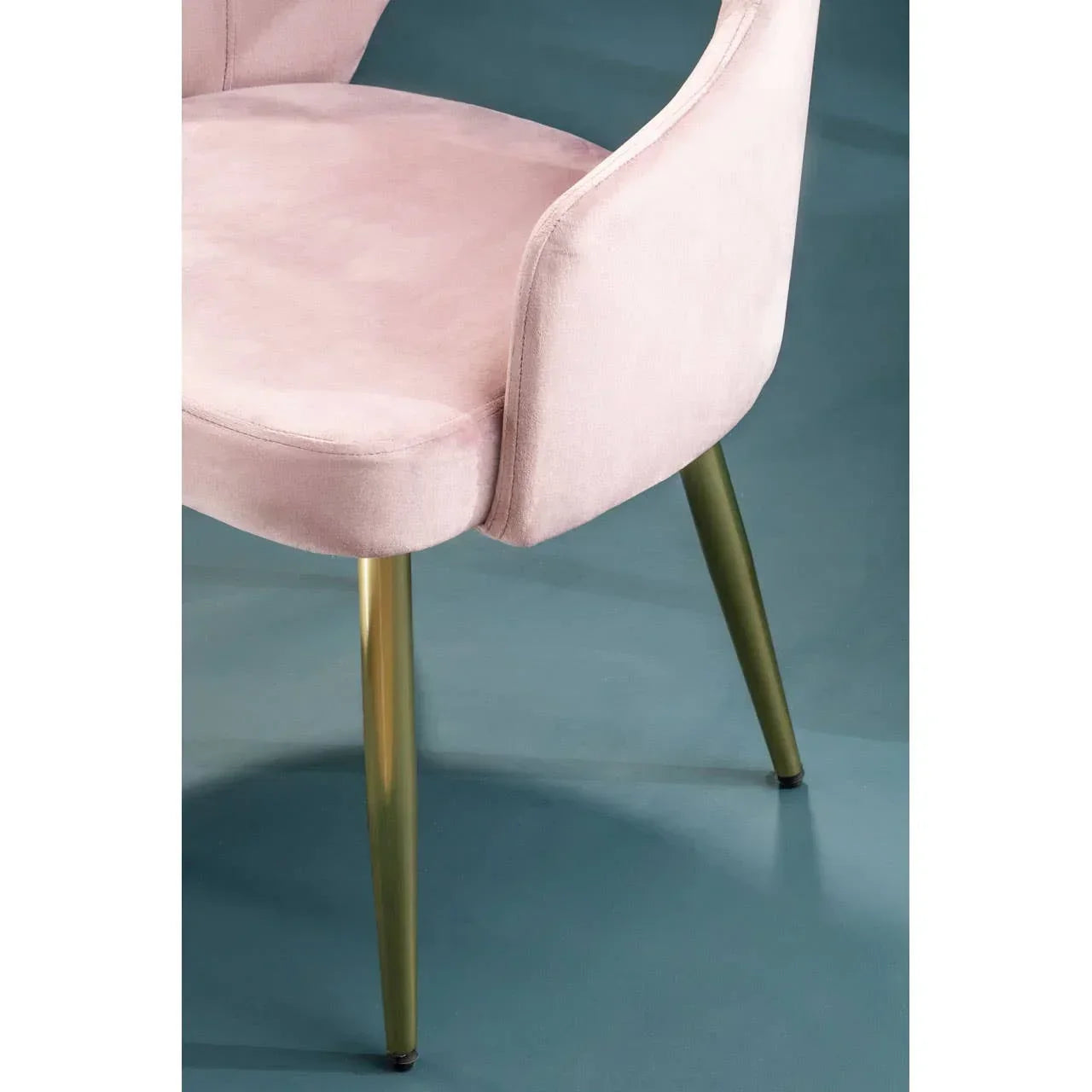 Blush pink velvet dining chair with gold metal legs on blue floor