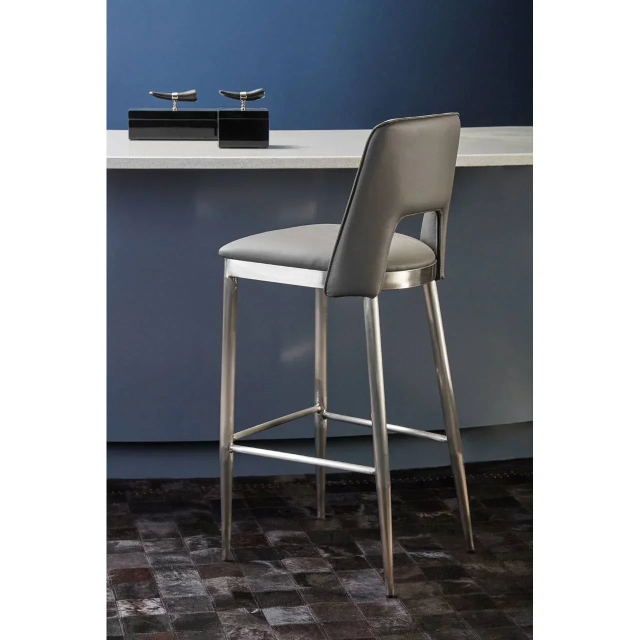 Grey bar stool with chrome legs at a white kitchen island on dark tiled flooring