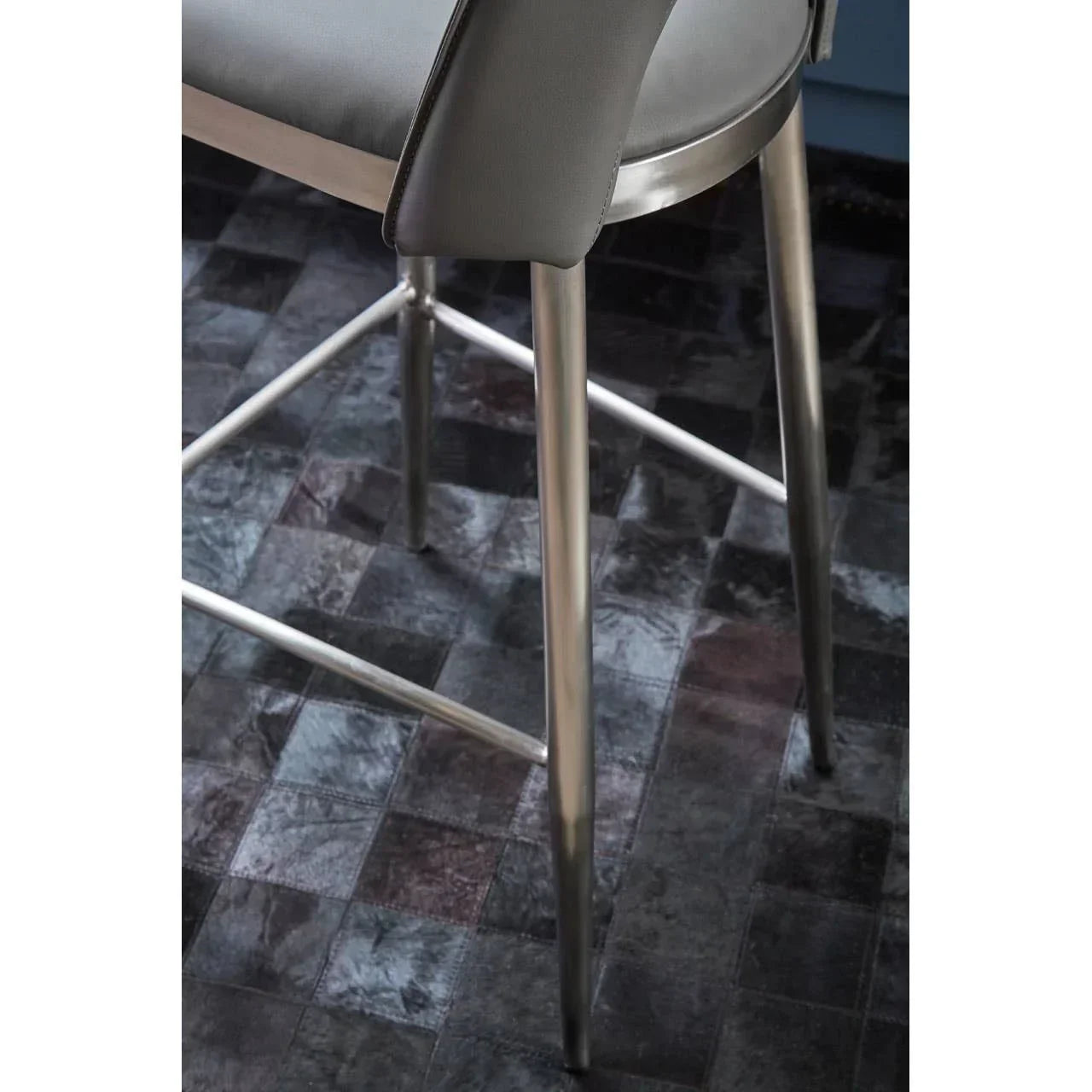 Grey upholstered bar stool with brushed metal legs on dark tiled floor