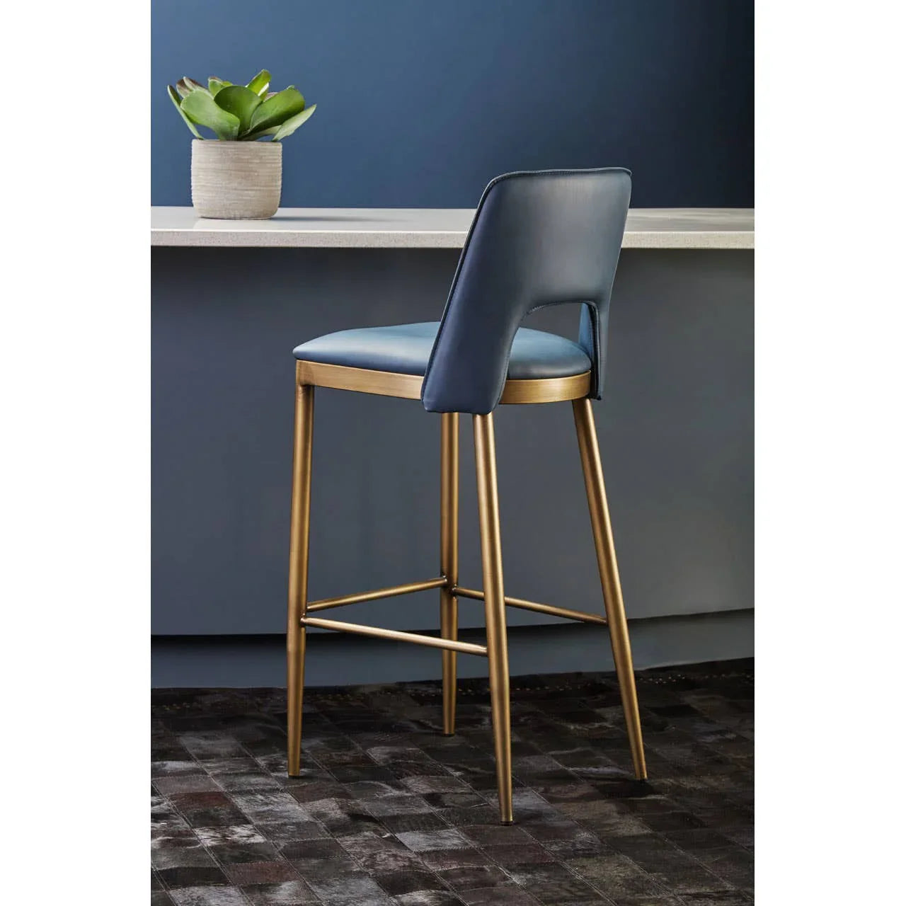 Blue upholstered bar stool with gold metal legs beside modern counter and plant pot