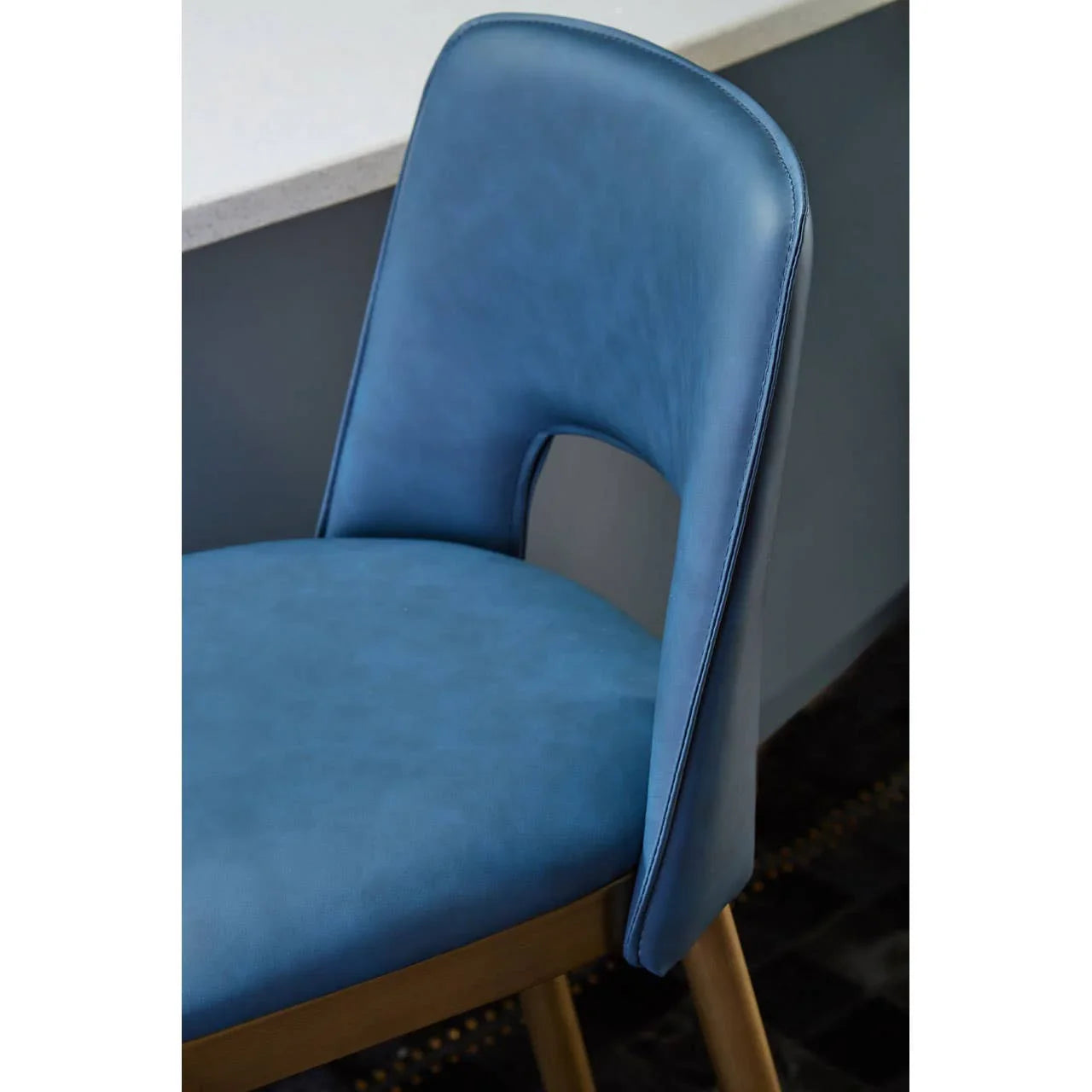 Blue faux leather dining chair with cut-out backrest and wooden legs beside counter