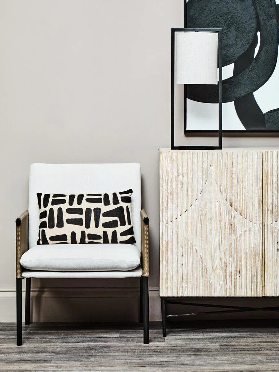 Modern accent chair with white cushion and patterned pillow beside textured wooden sideboard