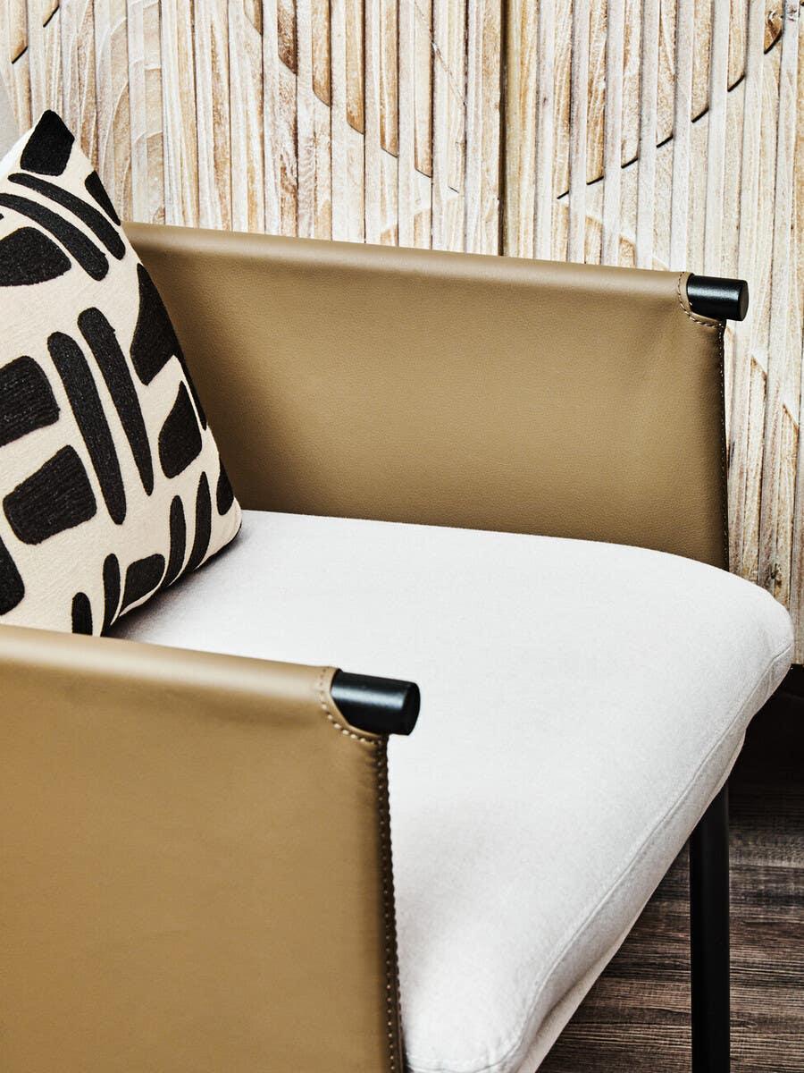 Tan leather armchair with white cushion and black patterned pillow in front of wood panel wall