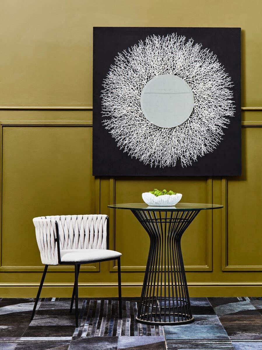 Modern glass dining table with black wire base and cushioned chair against olive wall