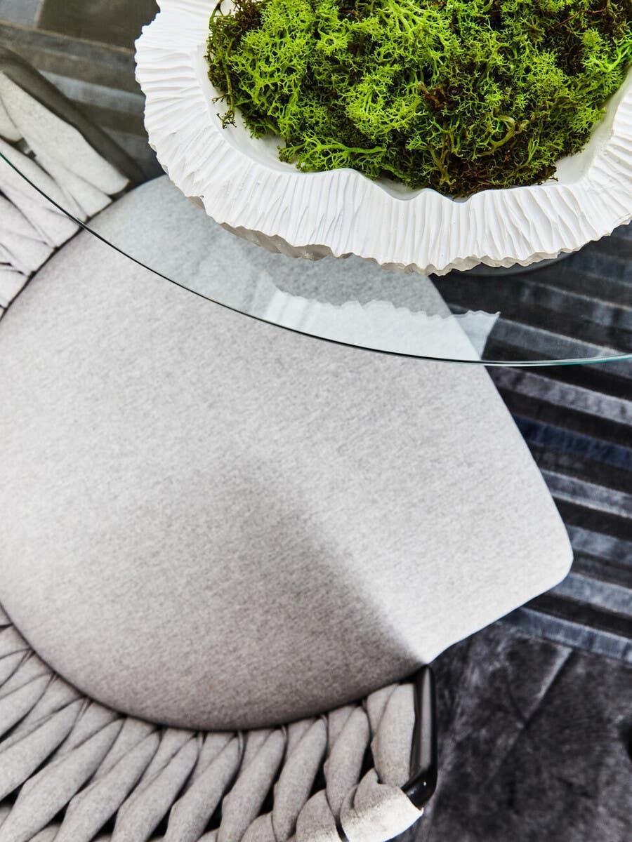 Glass dining table with white decorative bowl of green moss and grey upholstered dining chair