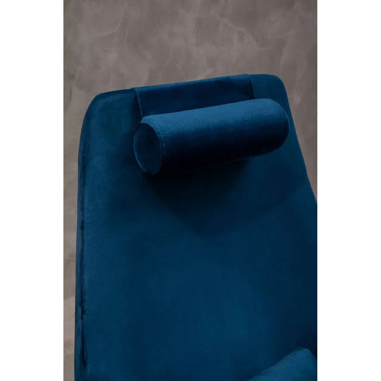 Close-up of blue velvet armchair with cylindrical headrest against grey wall