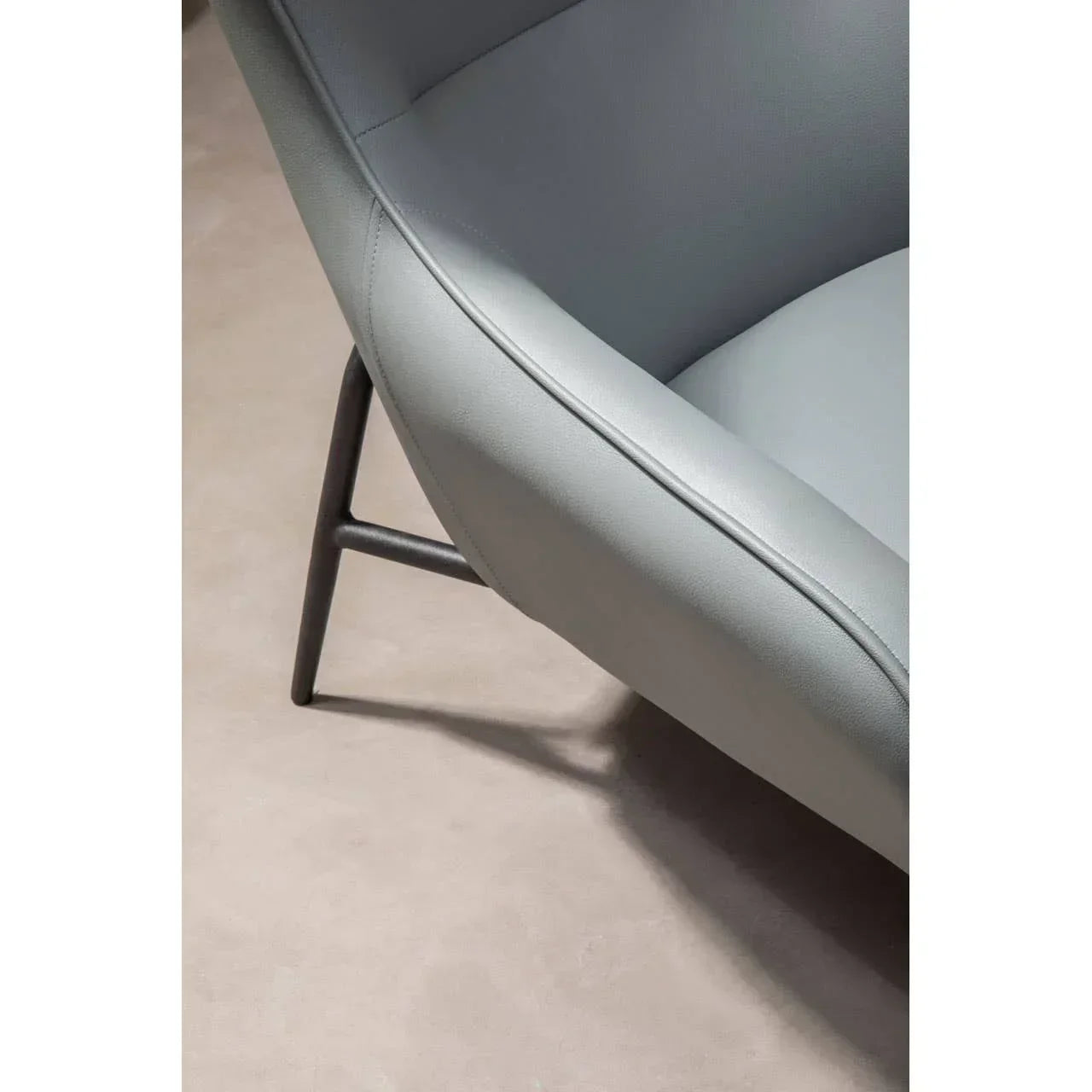 Close-up of grey leather chair upholstery with metal leg on beige floor