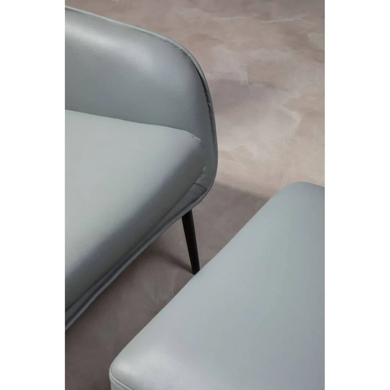 Close-up of modern grey leather sofa seat with matching ottoman on neutral floor