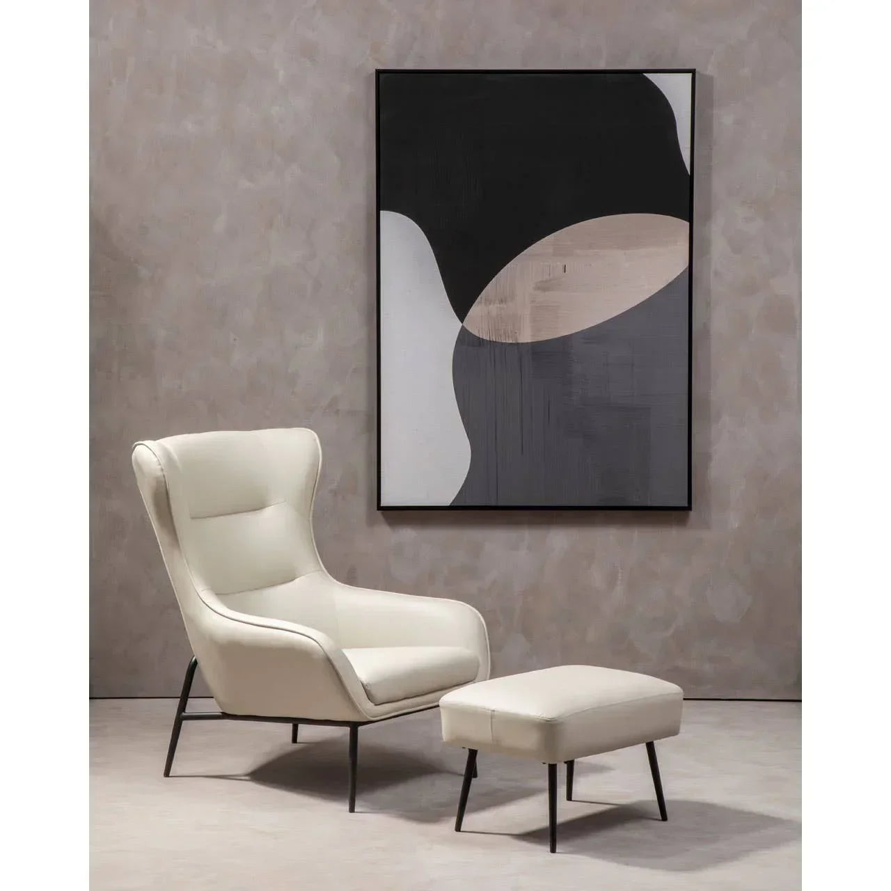 Cream armchair with matching ottoman and black legs beside abstract wall art in living room