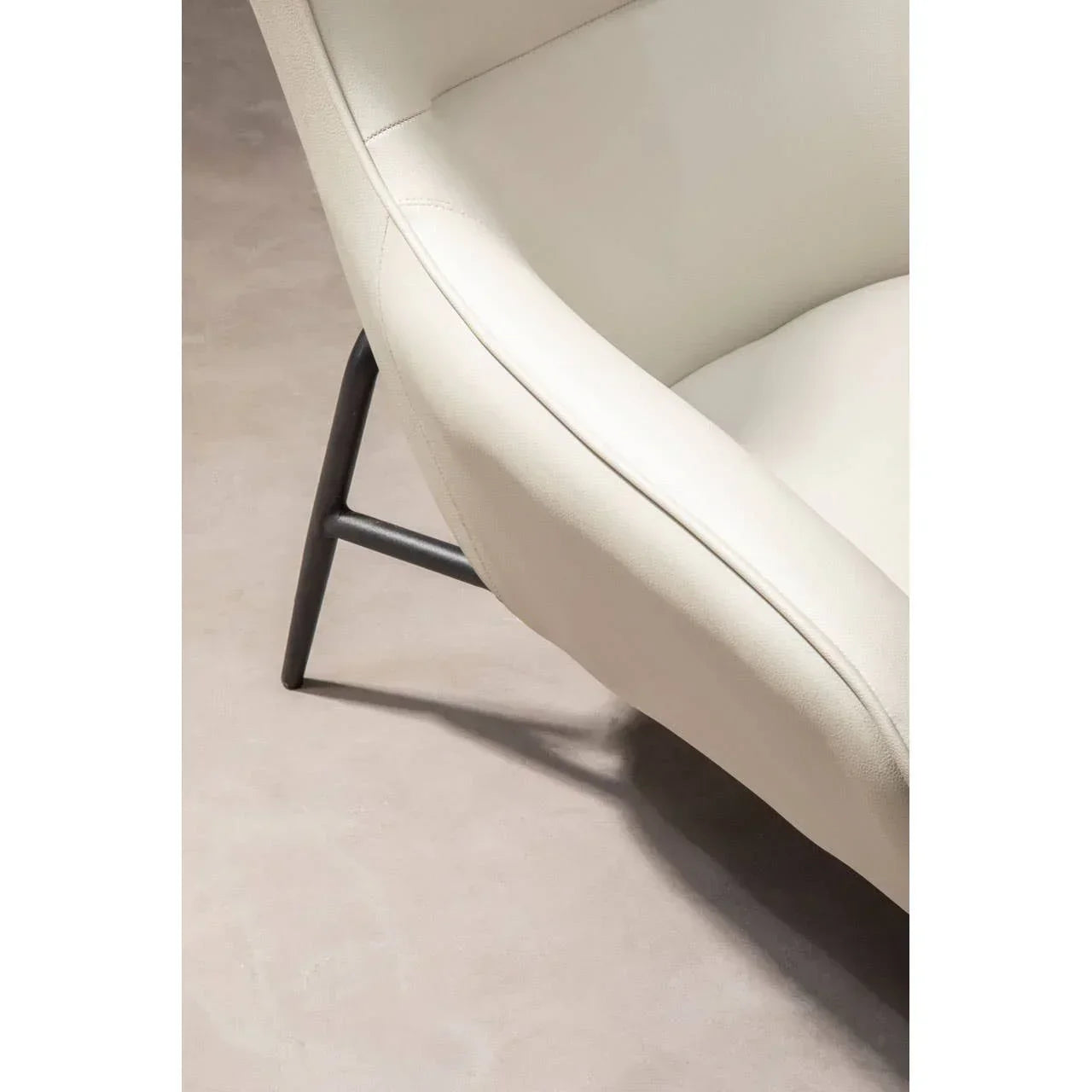 Close view of cream upholstered armchair with black metal legs on neutral floor