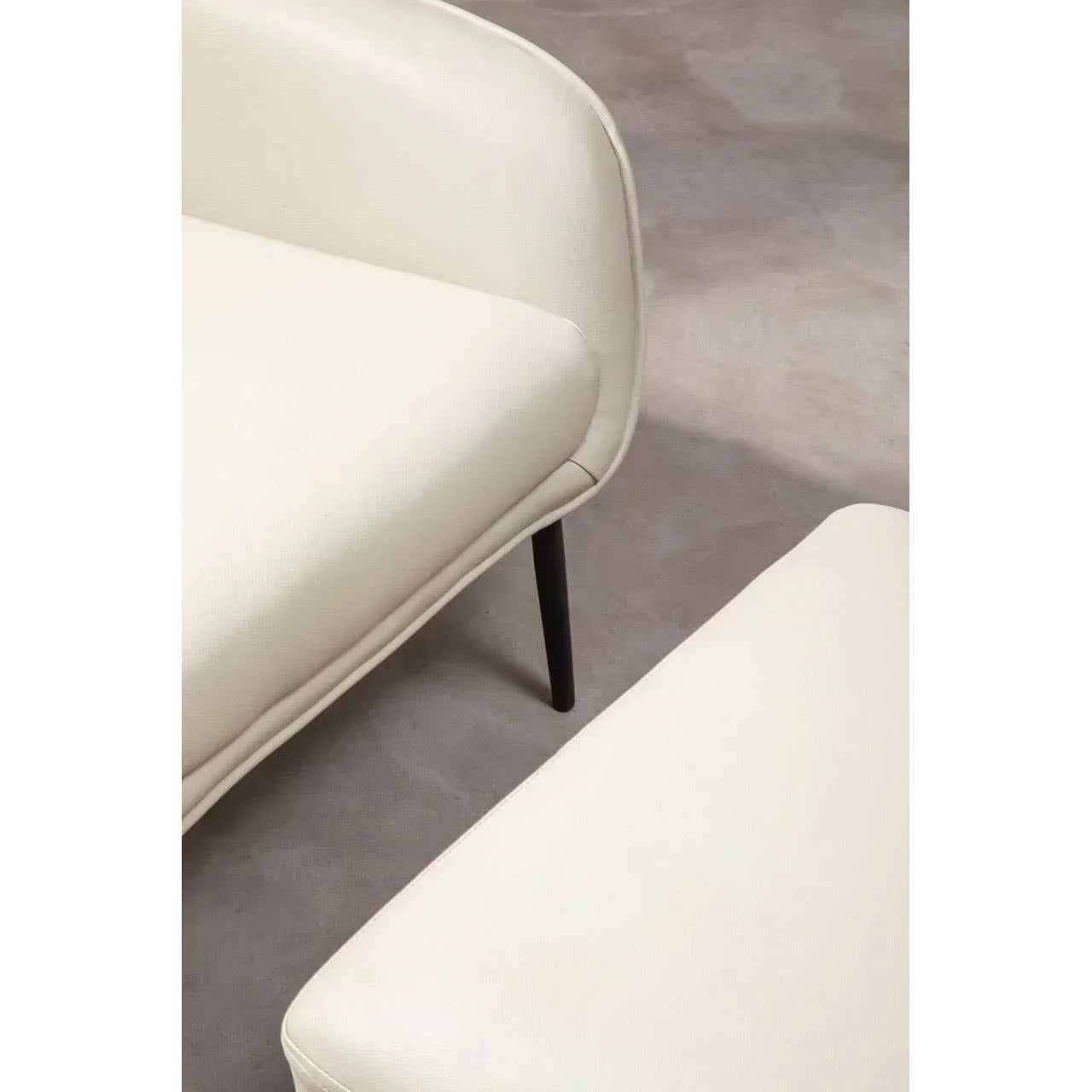 Cream fabric sofa and footstool with black metal legs on concrete floor