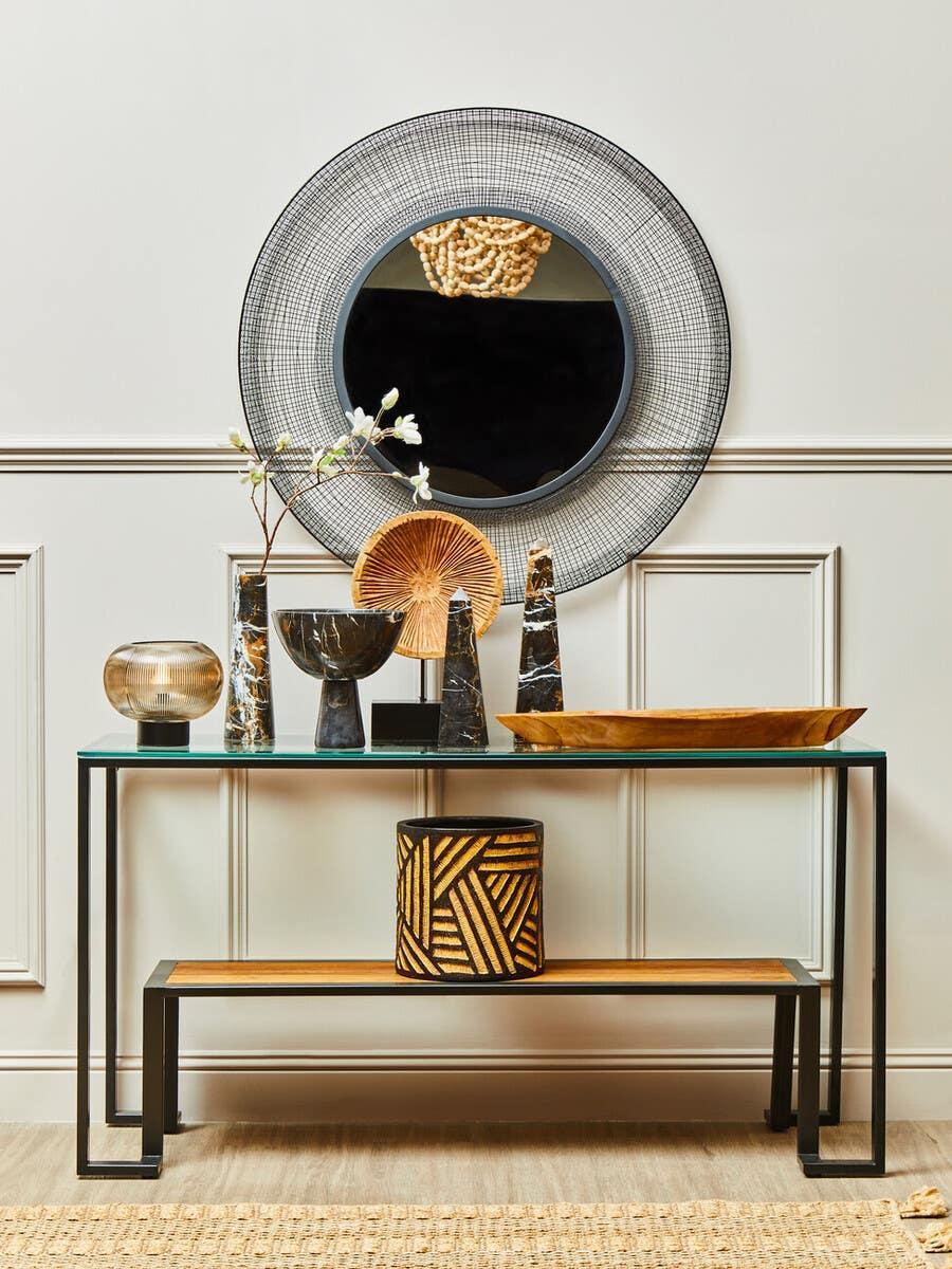 Glass console table with black metal frame, decorative vases and round wall mirror