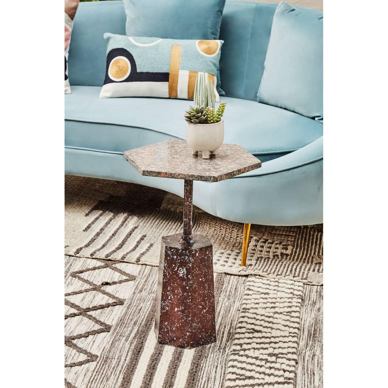 Hexagon stone side table with metal base beside blue sofa on patterned rug