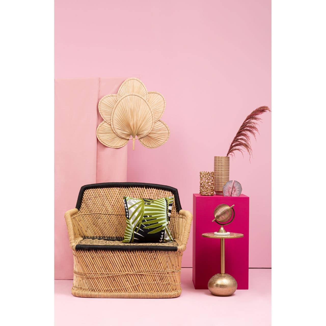 Natural rattan armchair with tropical cushion beside gold accent table and pink decor backdrop