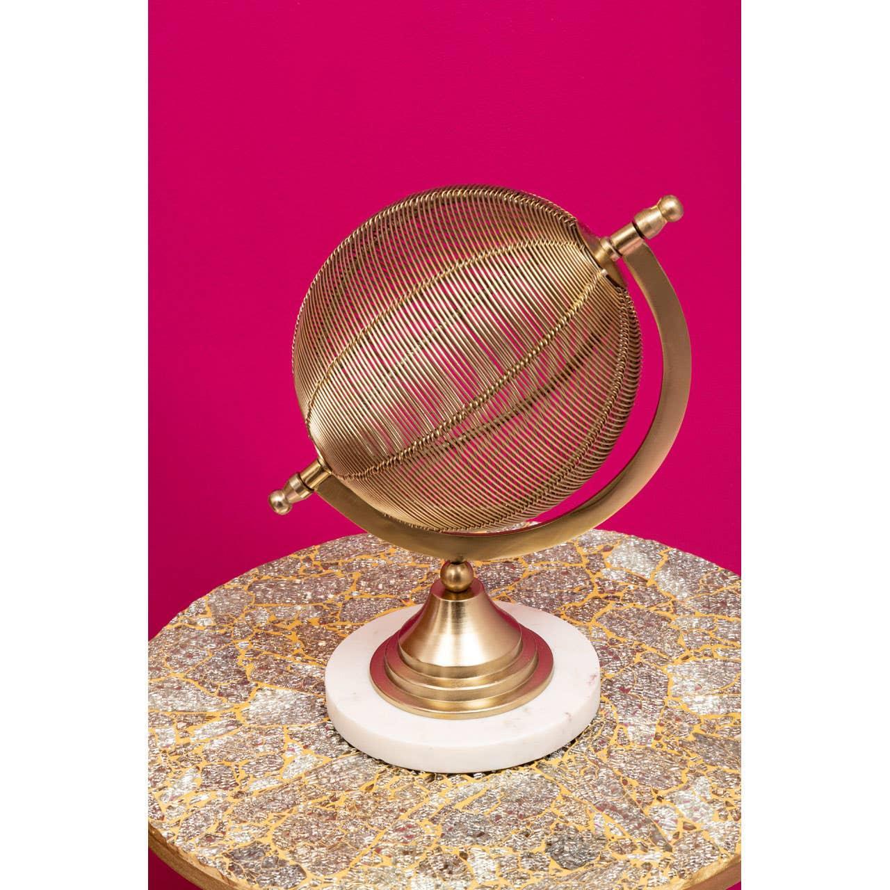 Gold wire globe ornament on marble and gold side table against pink background
